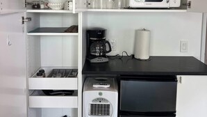 Een compacte keuken met witte kasten, een magnetron, een koffiezetapparaat en een koelkast.