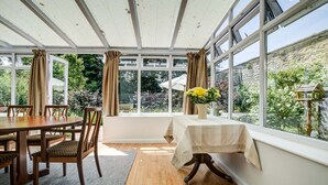 A dining area with a table and chairs, a vase with flowers, and large windows with curtains. - High Trees Blenheim View | Woodstock Holiday Let | 3 Beds & Sleeps 5 (Woodstock)