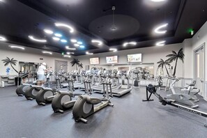 A gym with various cardio machines, a mirrored wall, and a ceiling with circular lights.