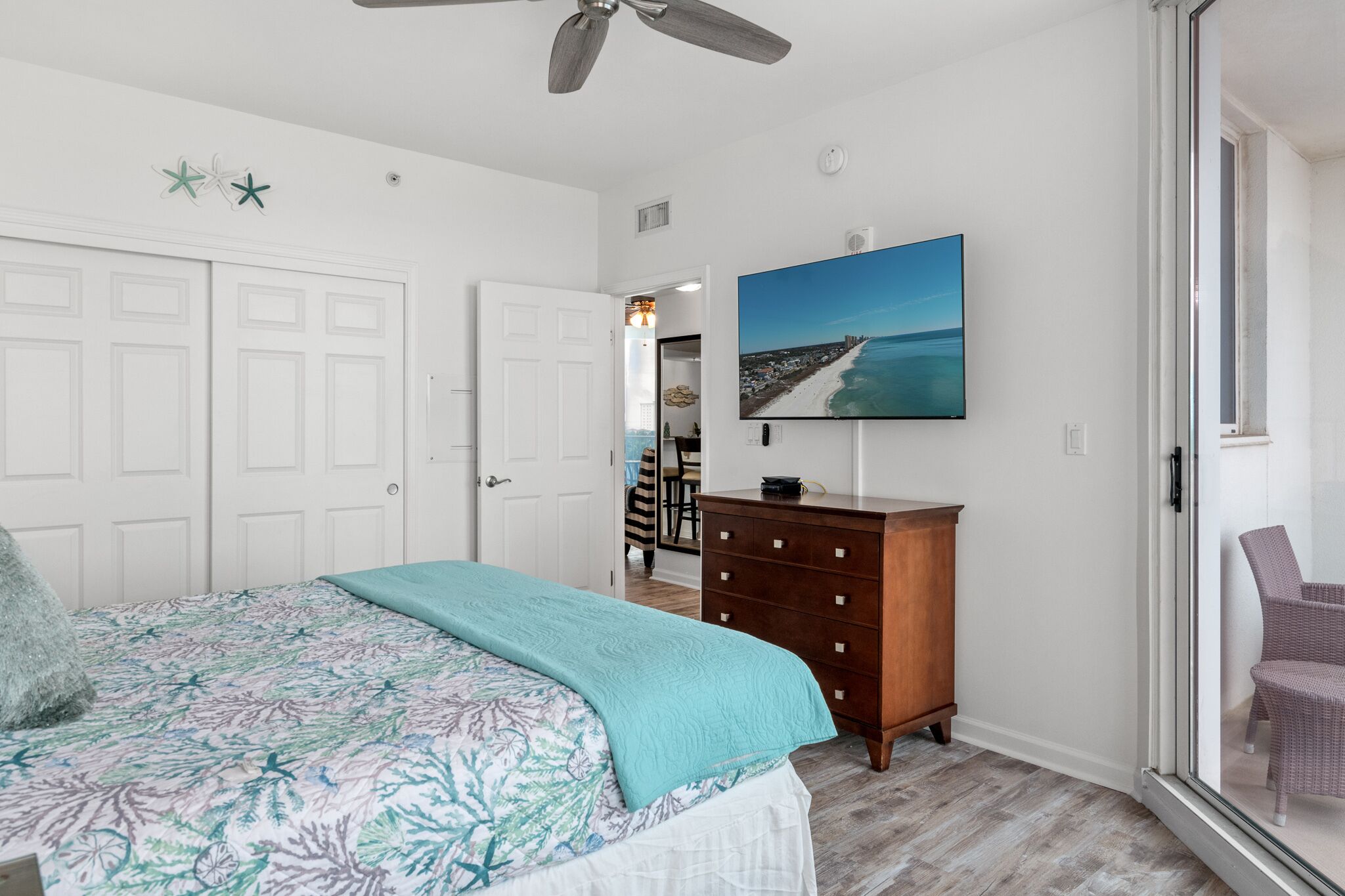 A bedroom with a bed, a dresser, a ceiling fan, and a painting of a beach scene.