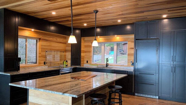 Een moderne keuken met een houten plafond, donkere kastjes en een centraal eiland met krukken.