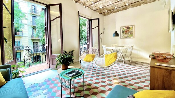 A room with a checkered floor, a sofa, a table with a magazine, a potted plant, and a view of the outside balcony. - Tyche Apartment Barcelona (Barcelona)