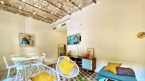 A living room with a checkered floor, white wicker chairs with yellow cushions, a blue sofa with a yellow pillow, and a small table with a book. - Tyche Apartment Barcelona (Barcelona)