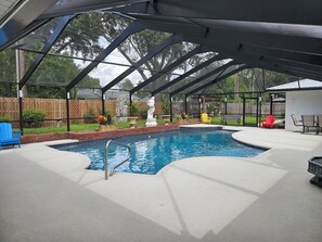 A covered outdoor swimming pool with a metal ladder, surrounded by a wooden fence, and featuring outdoor furniture and decorative plants.