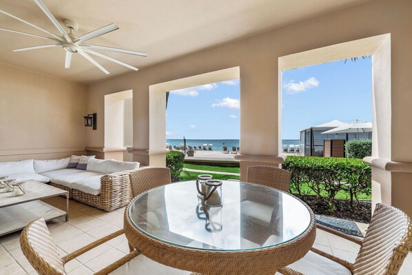 A balcony with wicker furniture, a glass table, and a view of the beach. - Incredible Oceanfront Oasis on 7 Mile Beach at The Ritz-Carlton (Seven Mile Beach)