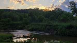 Un paisaje natural con un río, vegetación densa y un cielo despejado con rayos de sol.