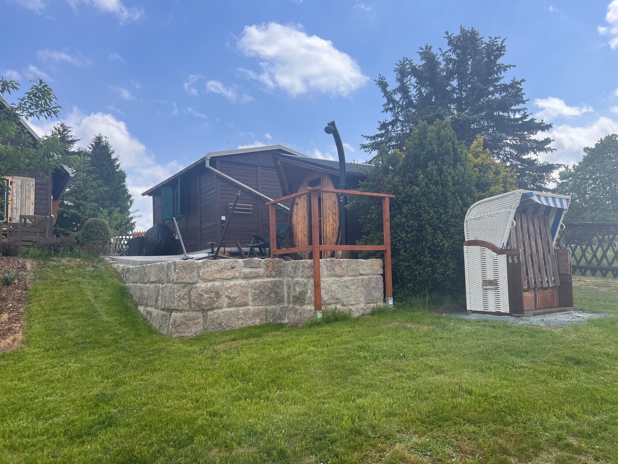 A wooden cabin with a stone foundation, a metal structure, and a small shed.