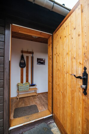 A wooden door leading to a room with a bench, a broom, and a mat.