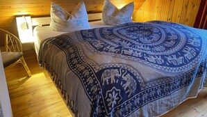 A bedroom with a wooden ceiling, a bed with patterned bedding, and a chair.
