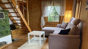 A cozy cabin interior with a wooden staircase, a sofa, a small table, and a window with curtains.