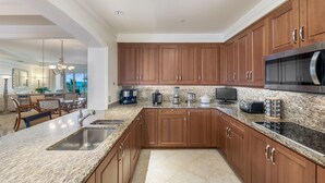 A modern kitchen with granite countertops, wooden cabinets, stainless steel appliances, and a dining area with a chandelier. - Private Residence at The Ritz-Carlton Resort, Grand Cayman (Seven Mile Beach)