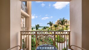 A balcony with wicker furniture and a glass table, overlooking a resort area with palm trees and a clear sky. - Private Residence at The Ritz-Carlton Resort, Grand Cayman (Seven Mile Beach)