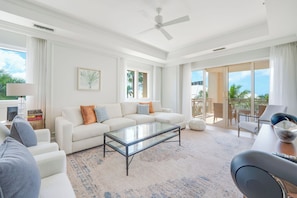 A spacious living room with a white sofa, a glass coffee table, and a view of the outdoors through large sliding doors.