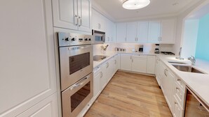 A modern kitchen with white cabinetry, stainless steel appliances, and a wooden floor. - Sophisticated Ocean View Residence located at The Ritz-Carlton (Seven Mile Beach)
