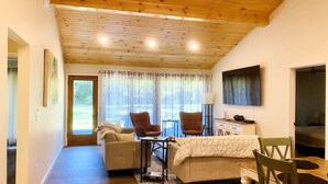 A cozy living room with a wooden ceiling, a sofa, two armchairs, a dining table with chairs, a TV, and a window with curtains. - Relax in our large 4b/2b ranch w/hot tub,firepit, game room, sleeps 11, pets ok (Sawyer)