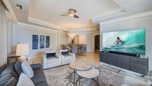 Ein modernes Wohnzimmer mit einem großen Flachbildfernseher, einem Deckenventilator und einem Essbereich im Hintergrund.