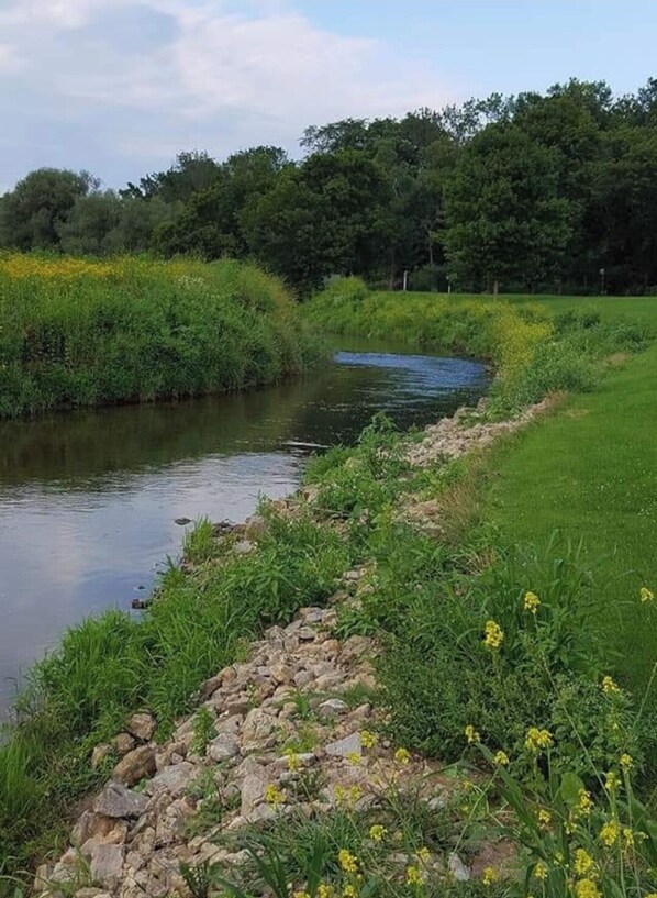 A river with a grassy bank and rocks. - Blakley Hobbit Campground-RV spot #1 (Viola)