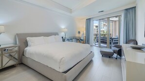 Moderni hotellihuone, jossa on suuri sänky, työpöytä tuolilla, pieni pöytä ja parveke, jolta on näkymä.