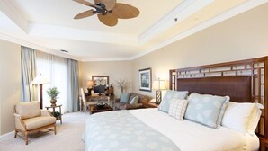 Une chambre d’hôtel avec un grand lit, une tête de lit en bois, un bureau avec une chaise, un canapé et un ventilateur de plafond.