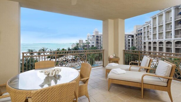 Un balcon agrémenté de meubles en osier, d’une table en verre et offrant une vue sur la plage et les bâtiments de l’hôtel.