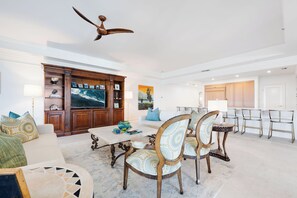 A spacious living room with a large flat-screen TV, a dining area with chairs and a table, and a ceiling fan. - Fantastic Large Oceanfront Residence Located at The Ritz-Carlton, Grand Cayma (Seven Mile Beach)