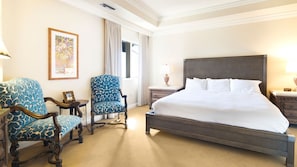 A hotel room with a large bed, two armchairs, a small table, and a painting on the wall.