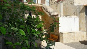 Un bâtiment doté d’un escalier menant à un balcon, entouré de verdure et agrémenté d’un banc.