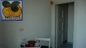 Un petit coin repas avec une table blanche, une chaise blanche, un bol, une tasse et un pichet. On aperçoit une porte au fond.