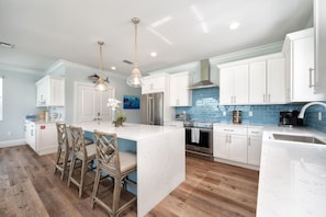 A modern kitchen with white cabinets, a marble island, and a blue backsplash.