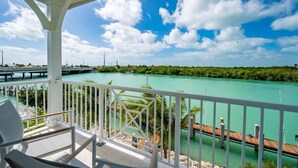 A balcony with a view of a turquoise river, a wooden dock, and a bridge in the distance.