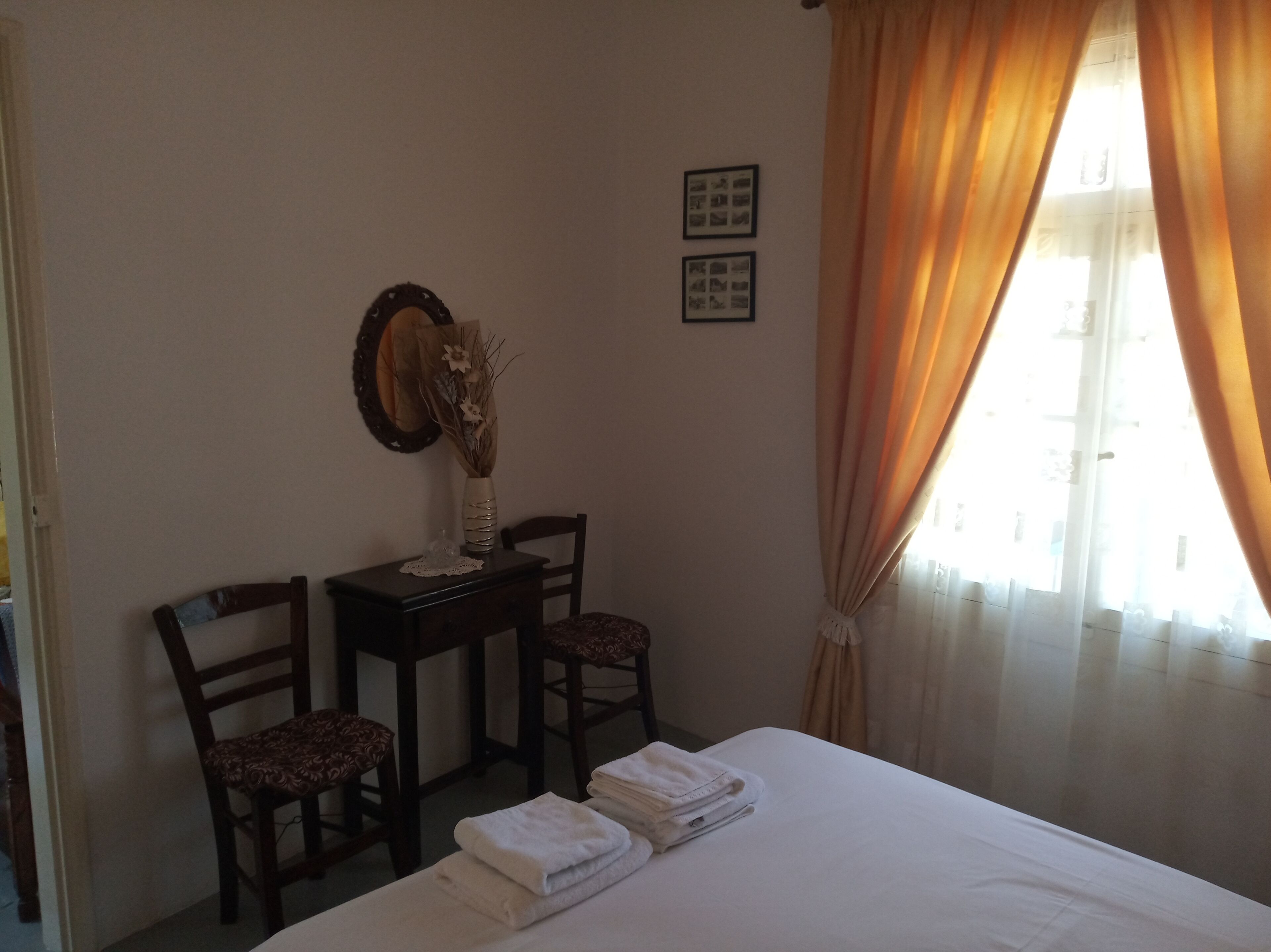 A hotel room with a bed, two chairs, a small table with a vase, and curtains.