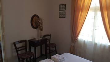 A hotel room with a bed, two chairs, a small table with a vase, and curtains.