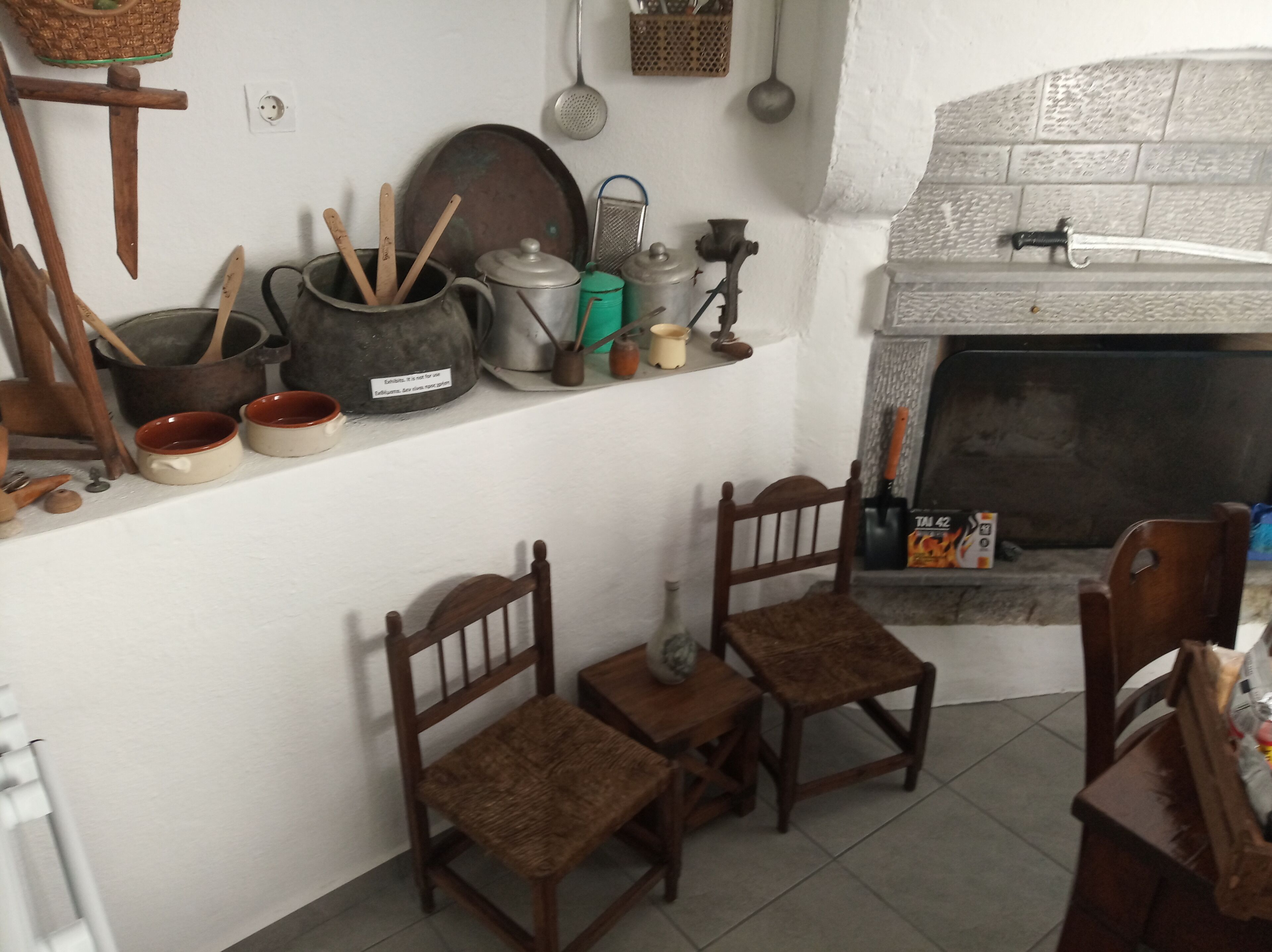 A rustic kitchen with wooden chairs, a fireplace, and various kitchen utensils.