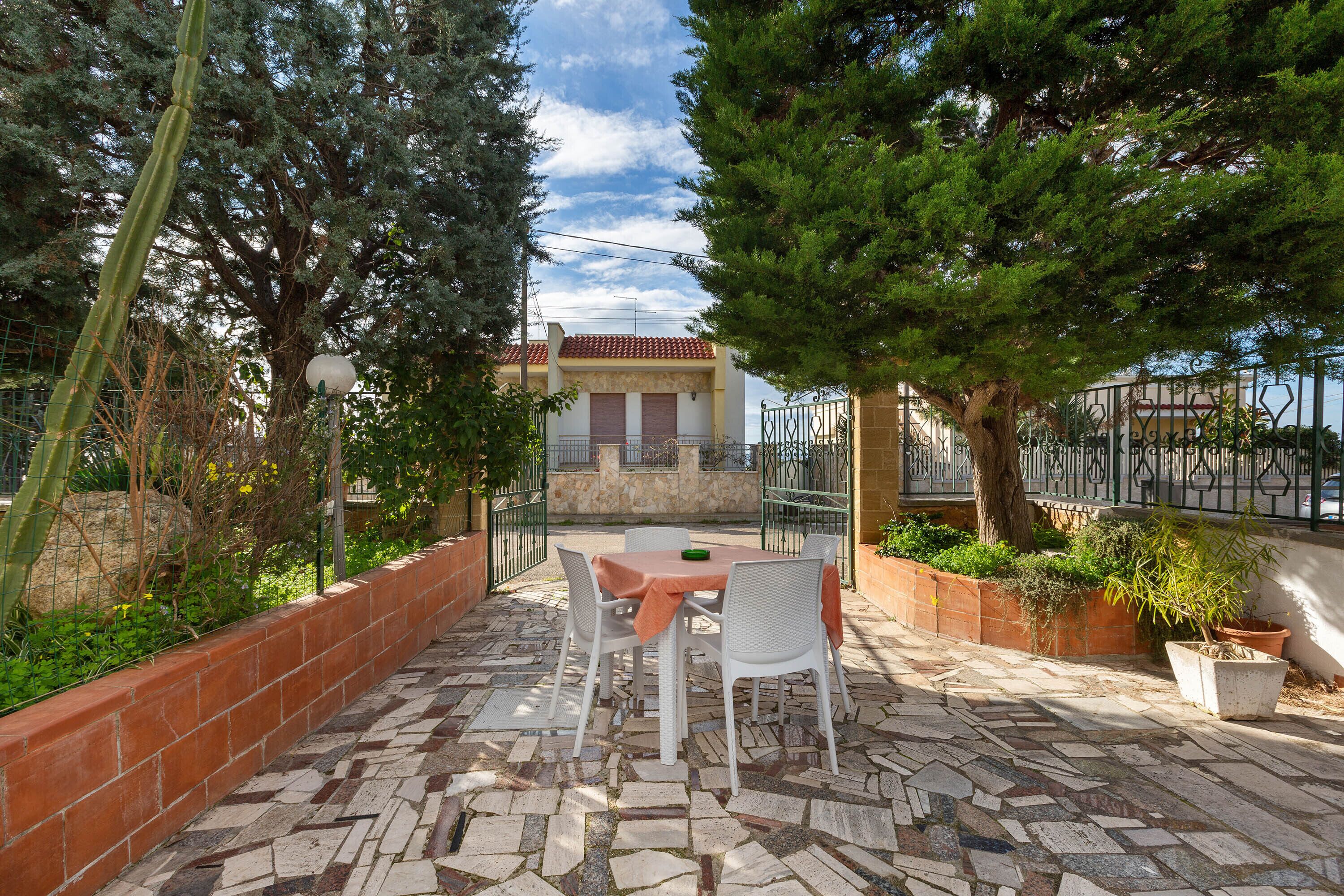 Un patio con tavolo e sedie, circondato da piante in vaso e un pavimento in pietra.