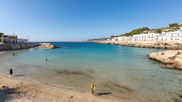 A coastal town with clear waters, a sandy beach, and white buildings along the shore.