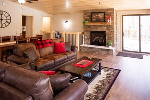 A living room with a stone fireplace, leather sofas, and a dining area with a wooden table and chairs.
