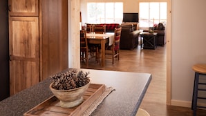 Una mesa de comedor de madera con sillas, un televisor al fondo y una zona de estar acogedora con un sofá y una mesa de centro.