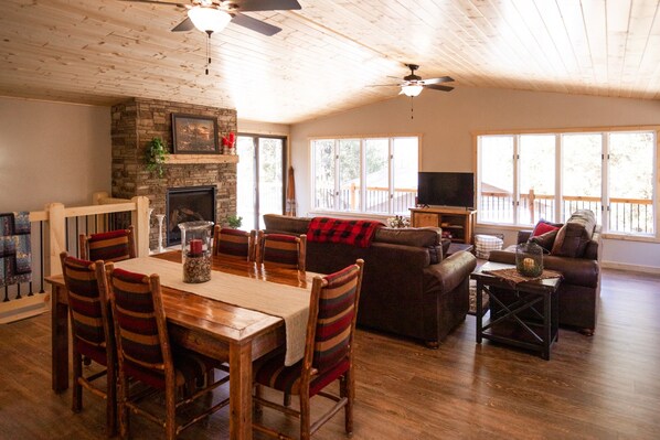 A spacious living room with a fireplace, wooden ceiling, and large windows.