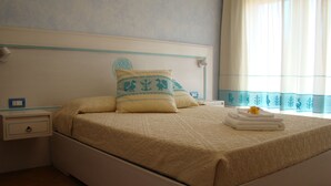 A neatly made bed with a patterned bedspread, a decorative pillow, and a folded towel with a rose on top.