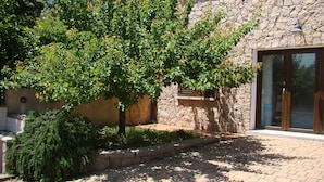 A stone building with a large tree in front, a paved walkway, and a window with a view of the outdoors.