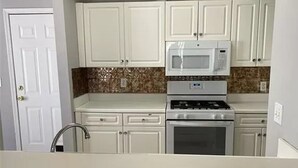 A compact kitchen with white cabinets, a microwave, and a stove. - cozy heaven (Sparks)