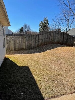 Backyard with a sloped grassy area leading to a wooden fence.