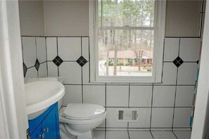 Bathroom features a toilet, blue cabinet, and a window with a residential view.