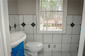 Bathroom features a toilet, blue cabinet, and a window with a residential view.