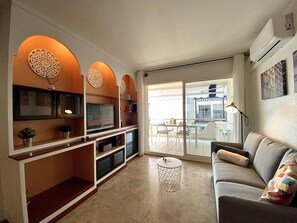 Un salon moderne avec un téléviseur, un canapé et un balcon équipé d’une table et de chaises.