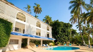 A hotel with a pool, palm trees, and a white building with balconies.