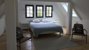Een slaapkamer met een bed, twee ramen, een stoel en een kleine tafel.