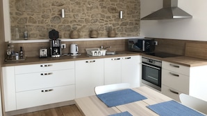 Een moderne keuken met een achterwand van natuursteen, witte kasten, een ingebouwde magnetron en een roestvrijstalen afzuigkap.