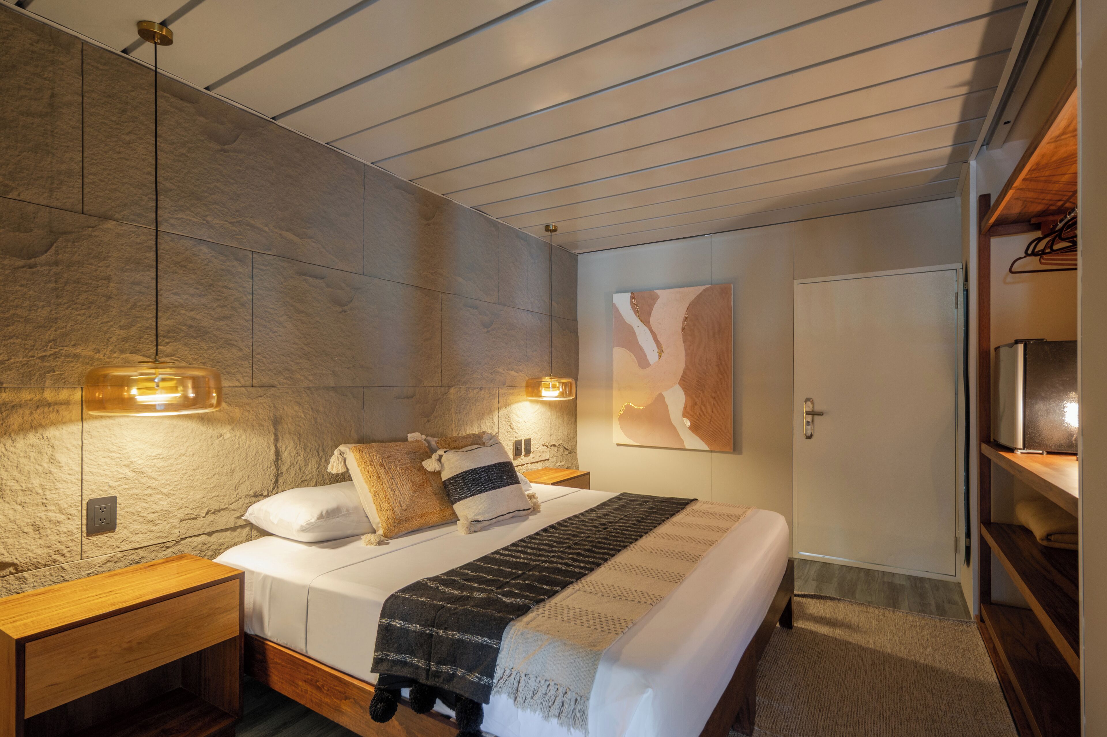 A modern bedroom with a large bed, two bedside tables, a wall-mounted light fixture, and a door with a coat rack.