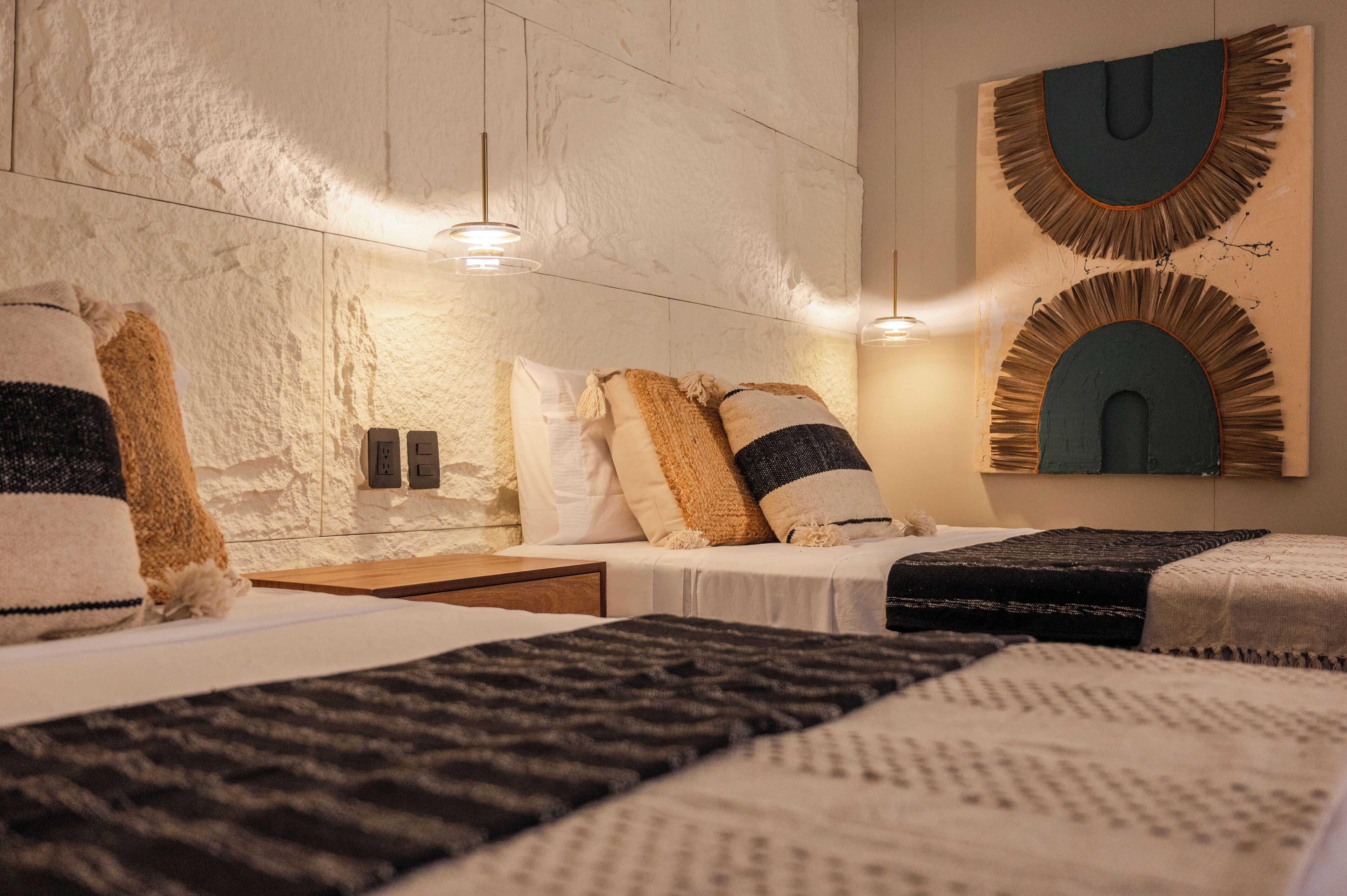 A hotel room with a marble wall, two beds with multiple pillows, and two pendant lights.